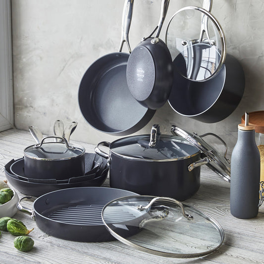 Thirteen-piece ceramic cookware set with glass lids arranged on a light wooden kitchen counter.