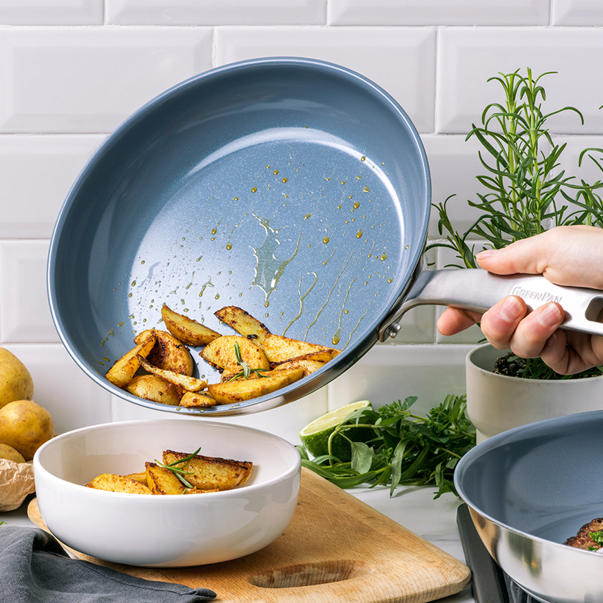 Potato wedges being poured from a stainless steel nonstick frypan into a white bowl.