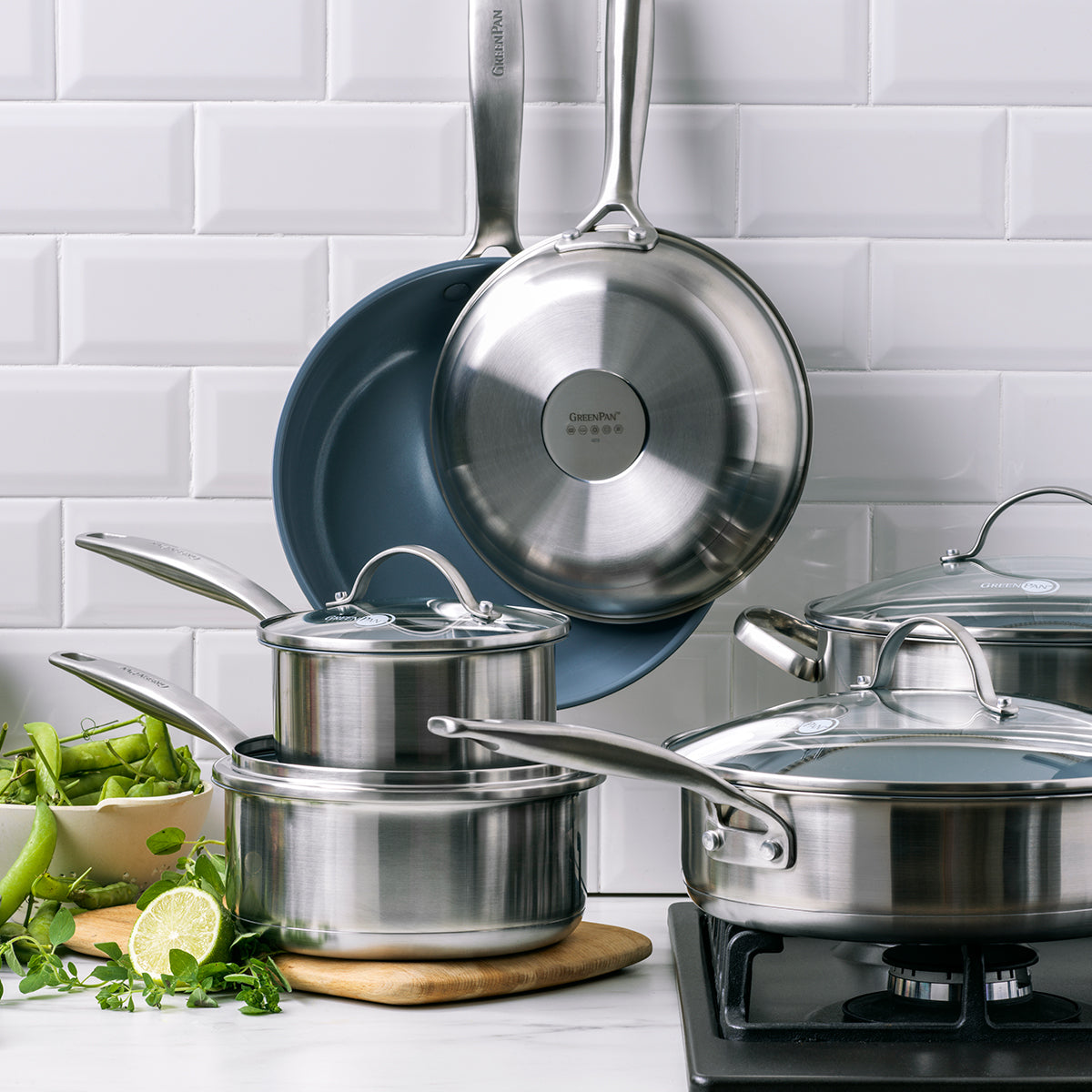 Stainless steel nonstick 10-piece cookware set with glass lids displayed on a stove with white tile backsplash.