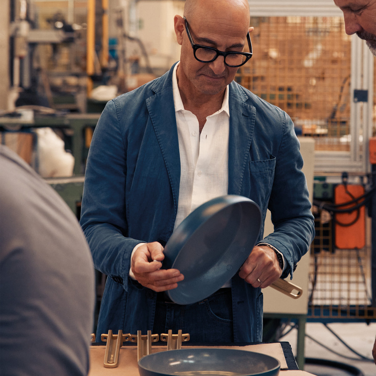 Stanley Tucci looking at a teal frypan in an industrial setting