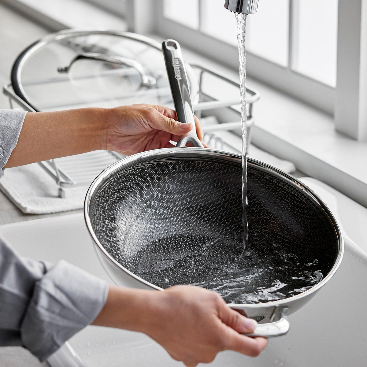 Hybrid ceramic nonstick wok with lid being rinsed in a kitchen sink.