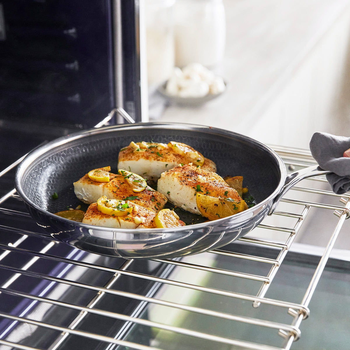 Fish fillets, potatoes, and herbs cooked in a white ceramic nonstick skillet.