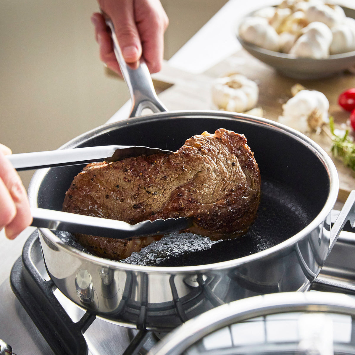 Steak being seared with herbs and garlic in a black ceramic nonstick frying pan on a stovetop.