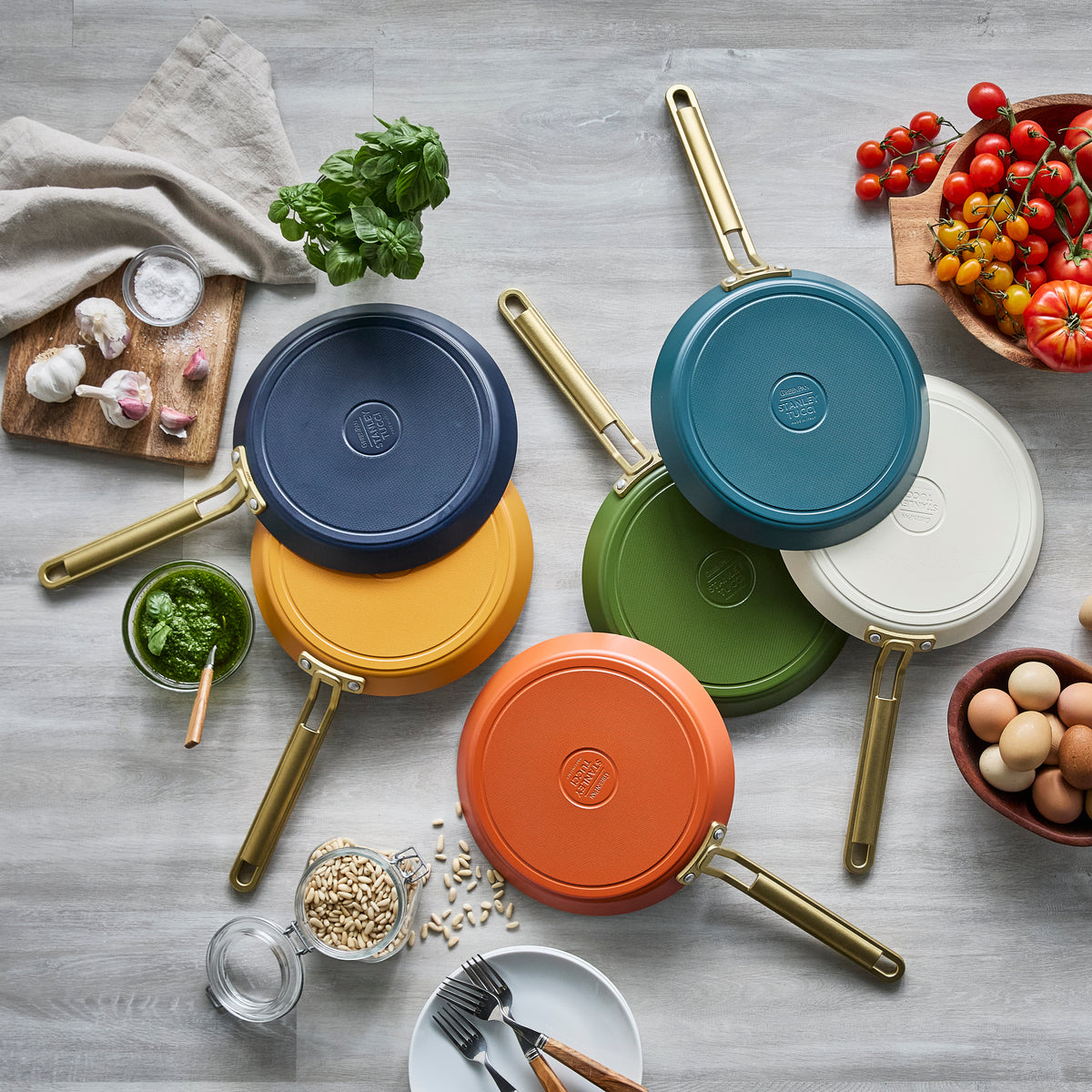 Colorful crepe pans on a wooden surface with ingredients and utensils.
