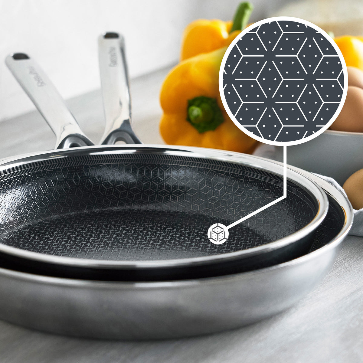 Hybrid ceramic nonstick pans with a geometric pattern, yellow pepper and eggs in the background.