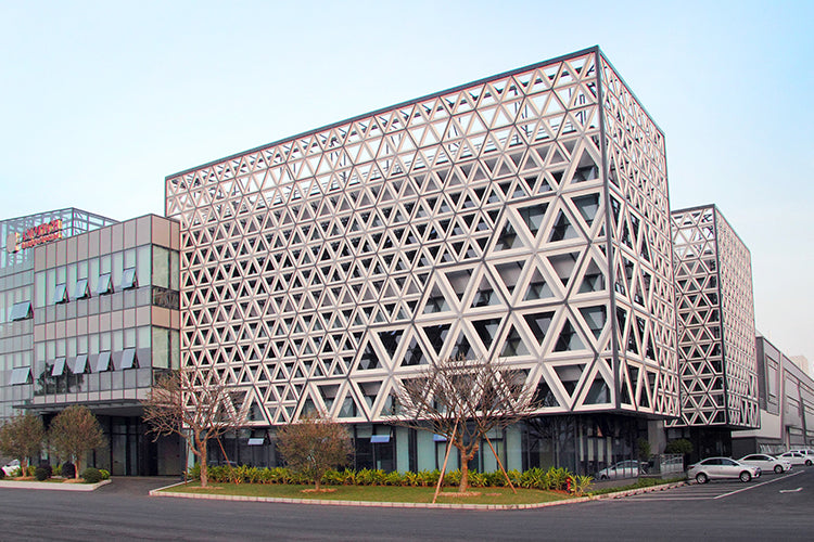 Cookware set displayed outside a modern building with large windows and a geometric, triangular-patterned facade on a clear day.