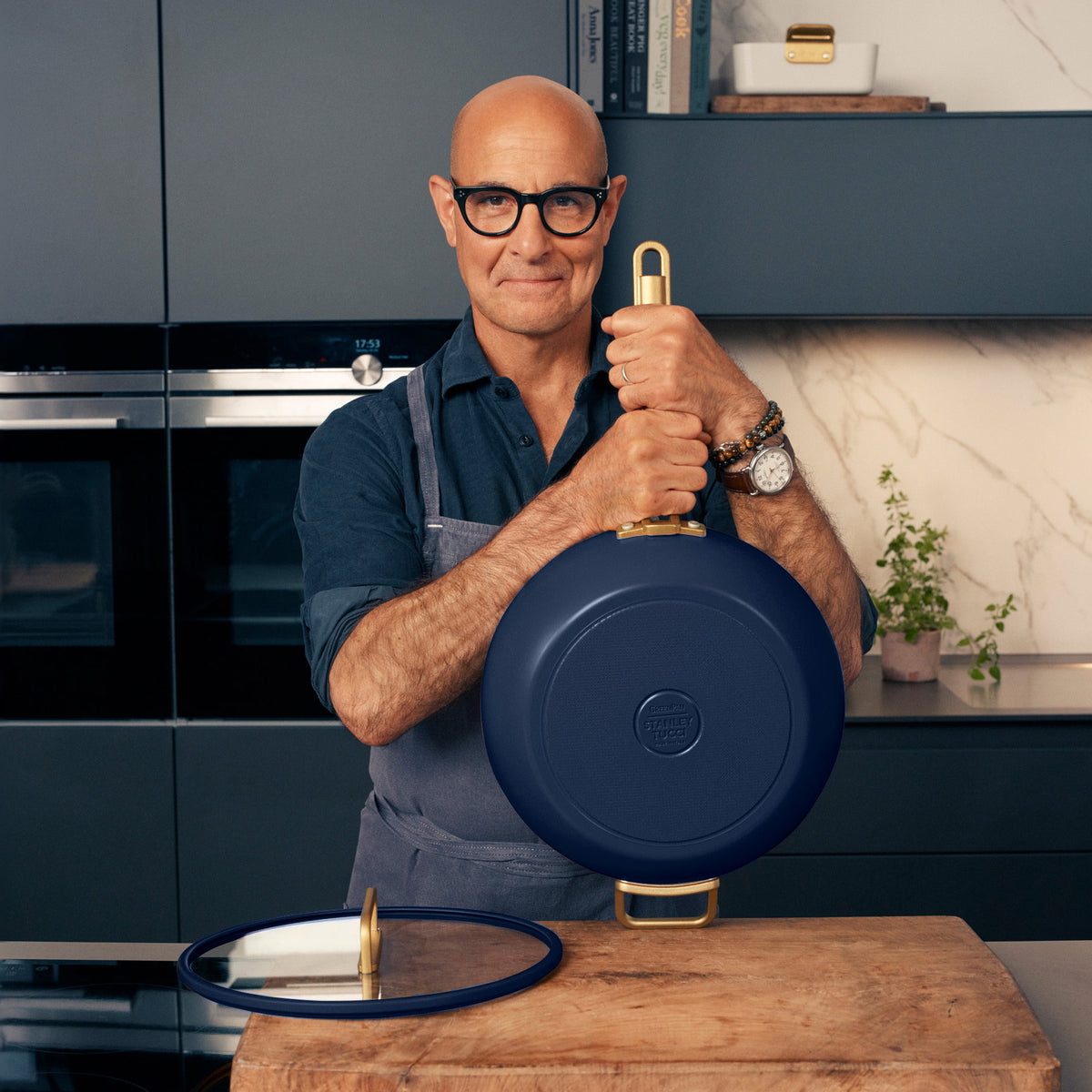 A man in glasses holds a blue ceramic Stanley Tucci 4.5-quart pan in a kitchen.