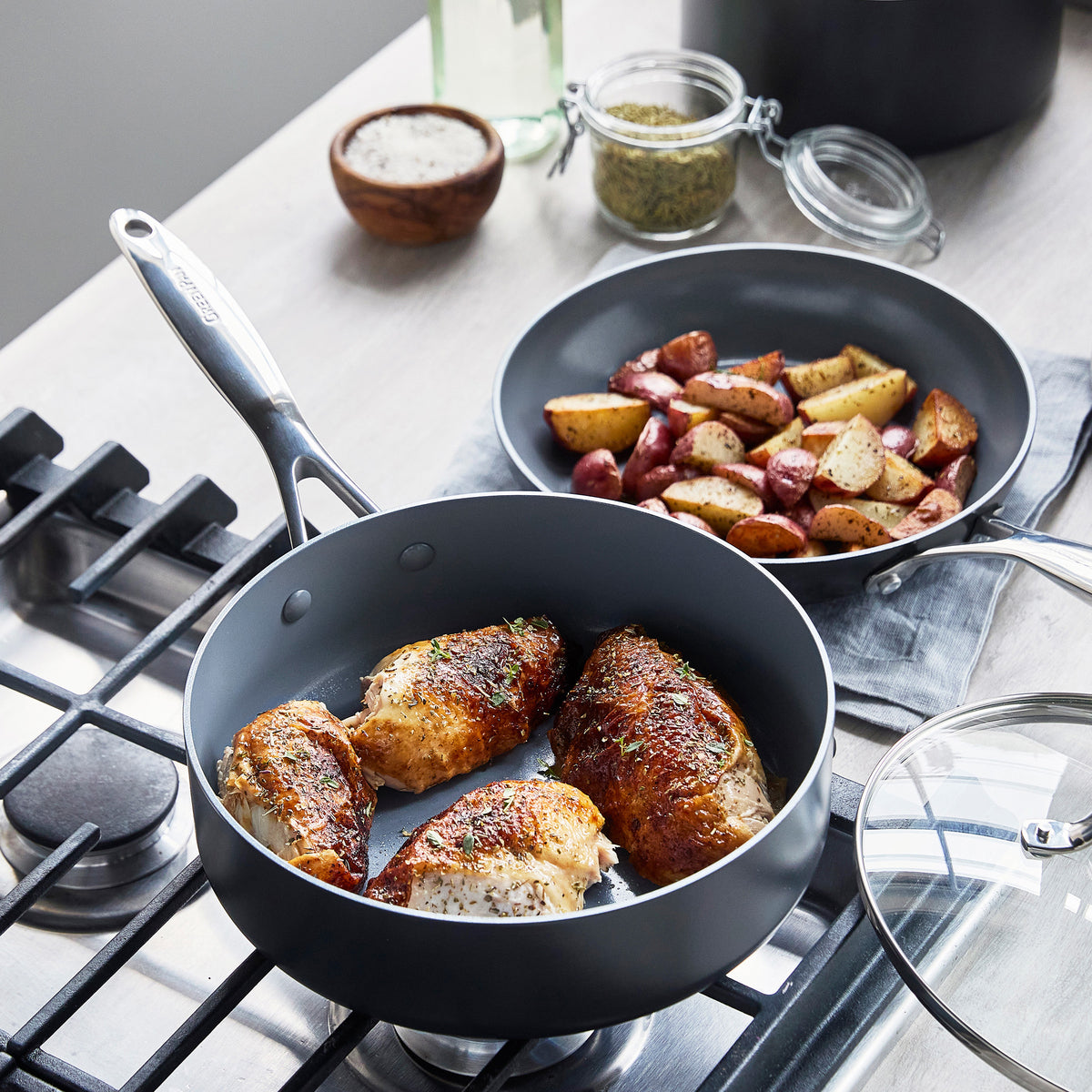 Chicken breasts cook in a gray ceramic skillet with roasted potatoes, from the Valencia Pro Cookware Set.