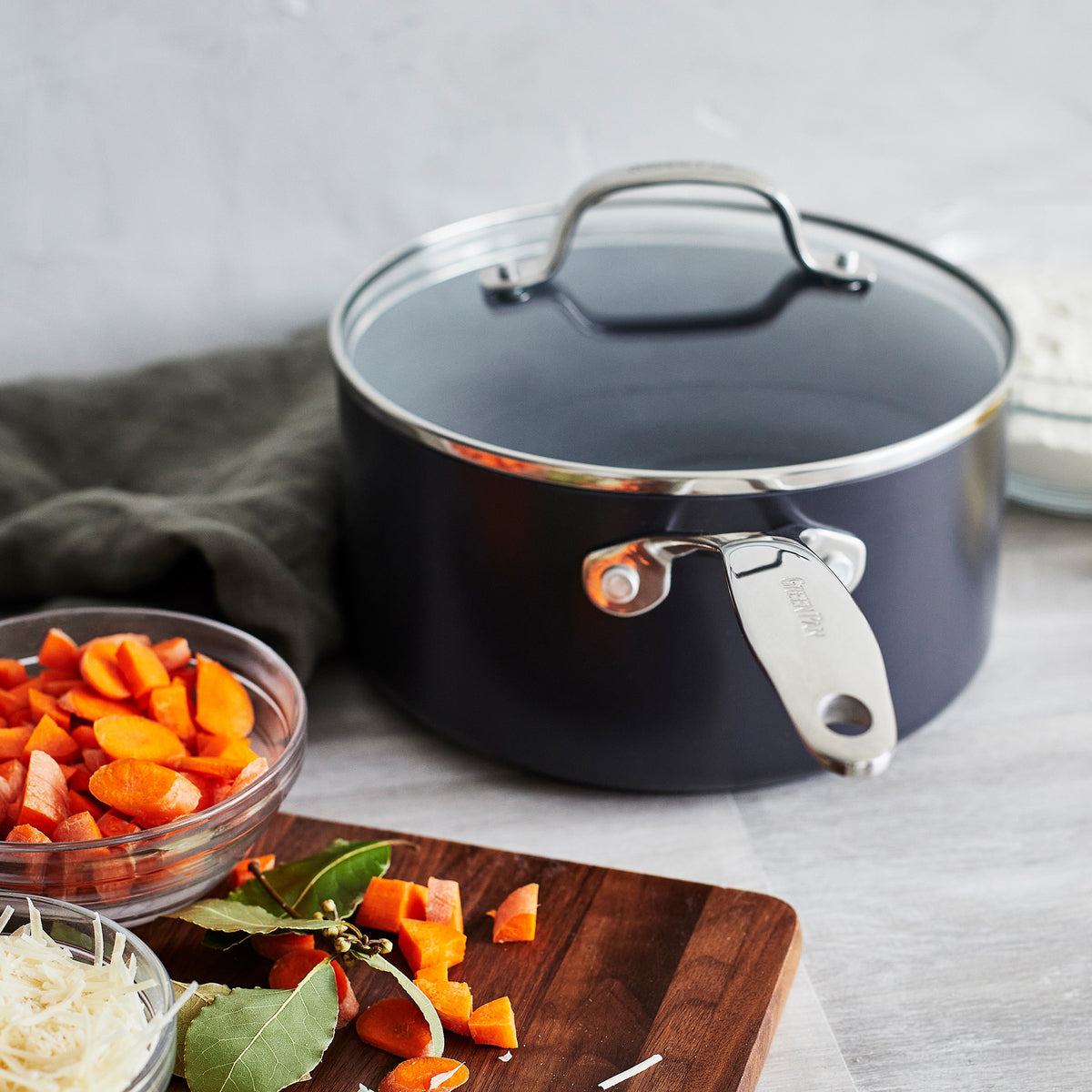 Ceramic nonstick frying pan next to chopped carrots, bay leaves, and shredded cheese on a kitchen counter.