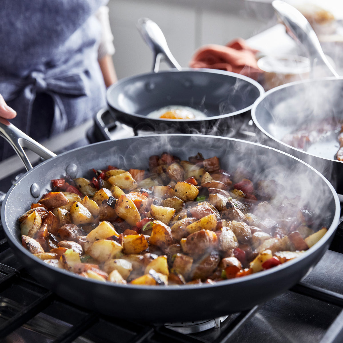 Roasted potatoes and vegetables in a gray ceramic nonstick frying pan on a stovetop.
