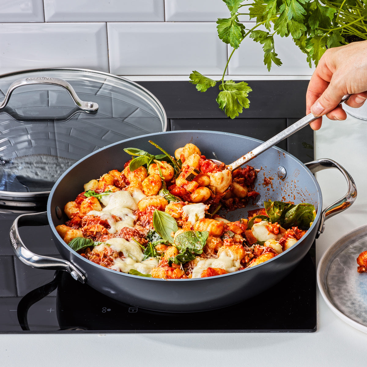 Cheesy gnocchi with spinach and tomato sauce being stirred in a gray ceramic nonstick skillet.