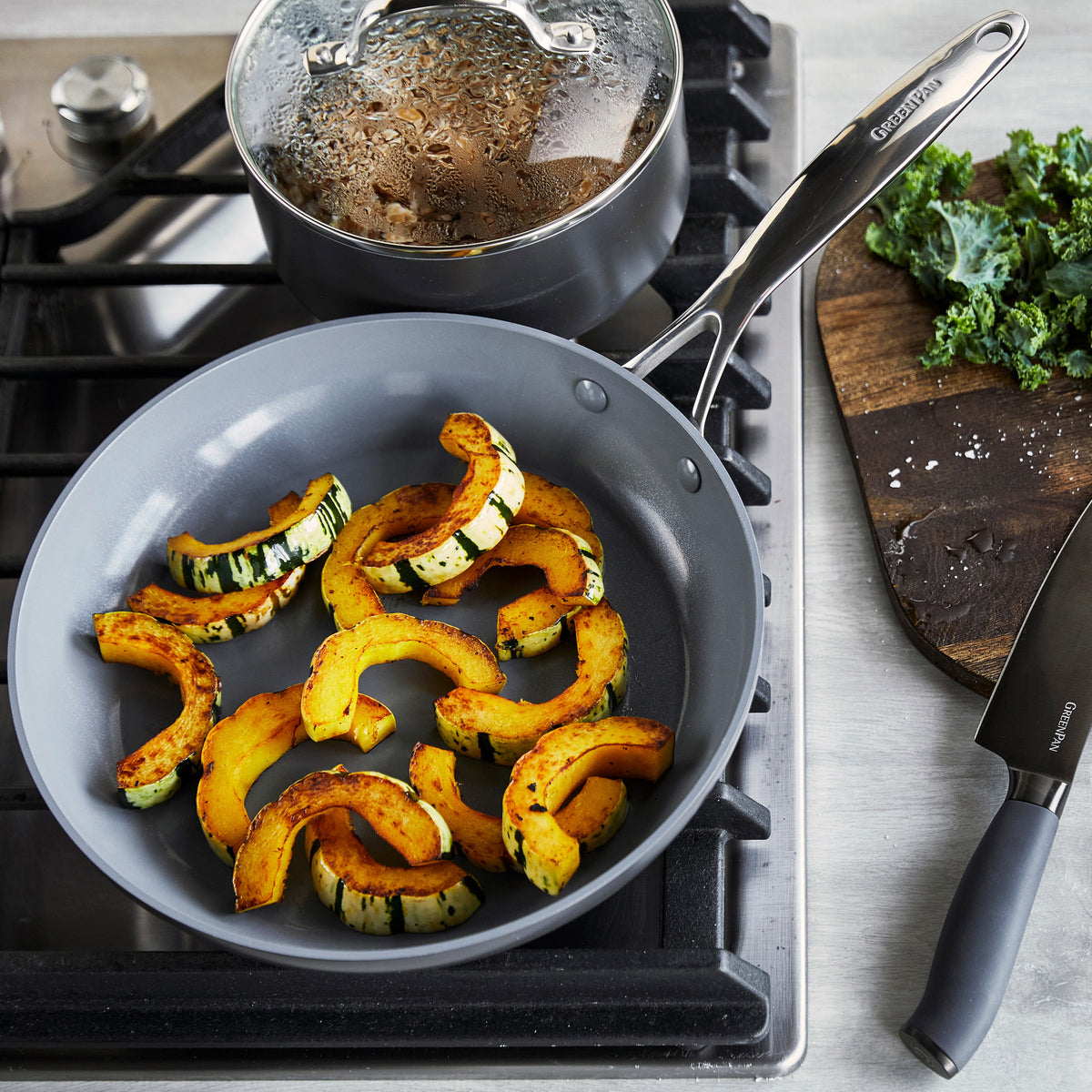 Yellow squash slices cooking in a gray ceramic frying pan, part of a 13-piece cookware set; kale sits beside the pan.