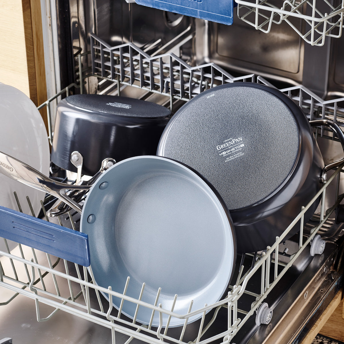Open dishwasher loaded with several pots and pans, including the Valencia Pro Ceramic Nonstick 1.5-Quart and 3-Quart Saucepan Set with Lids in gray. Its scratch resistance is ideal for everyday cleaning on the bottom rack.