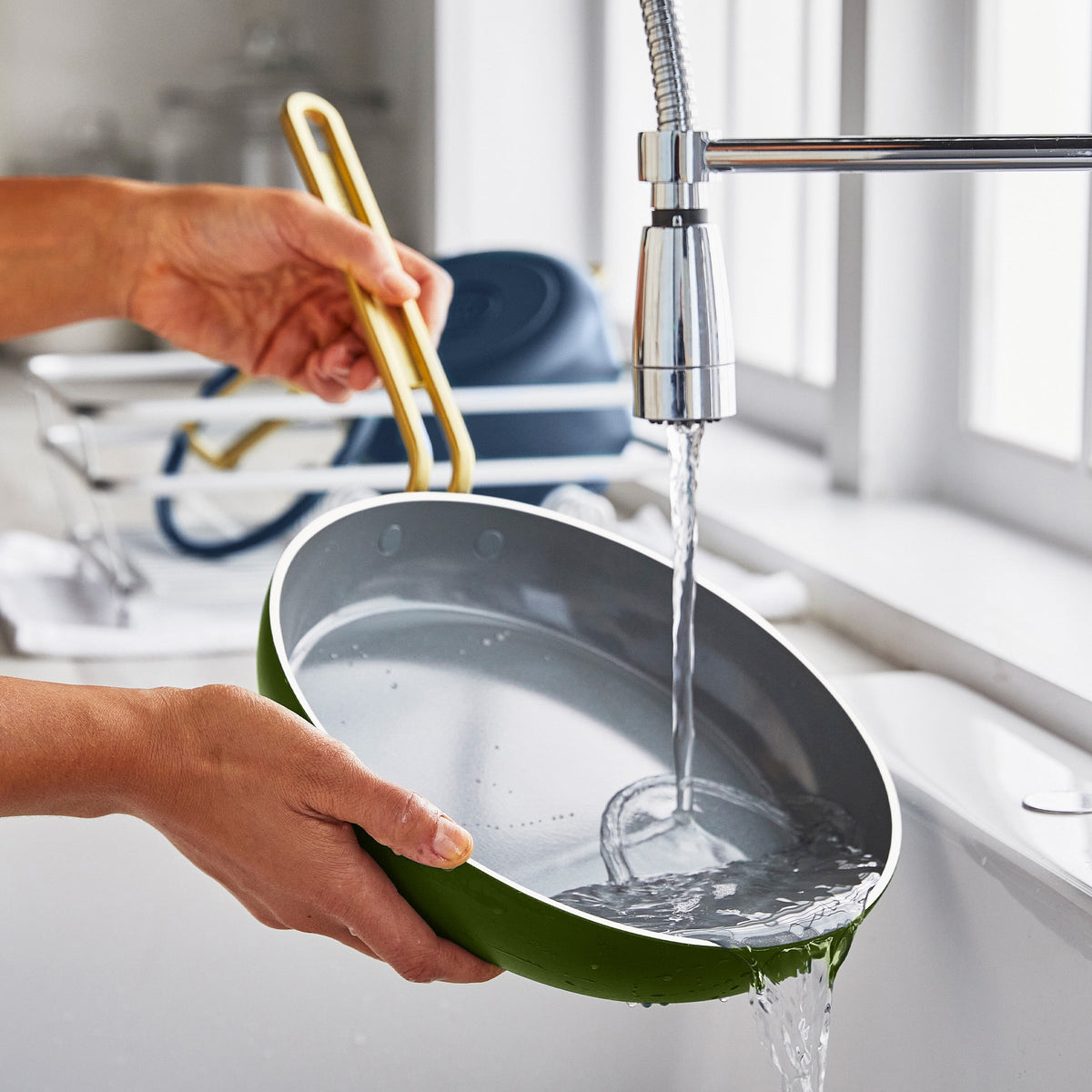 Person washing a green frypan under running water in a kitchen sink.