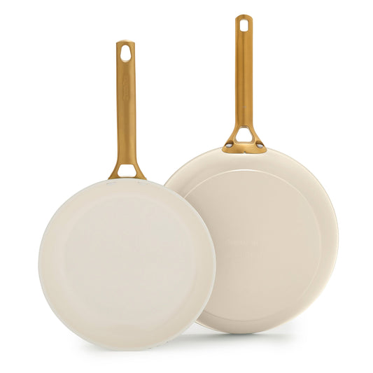 Two cream frying pans with gold handles on a white background