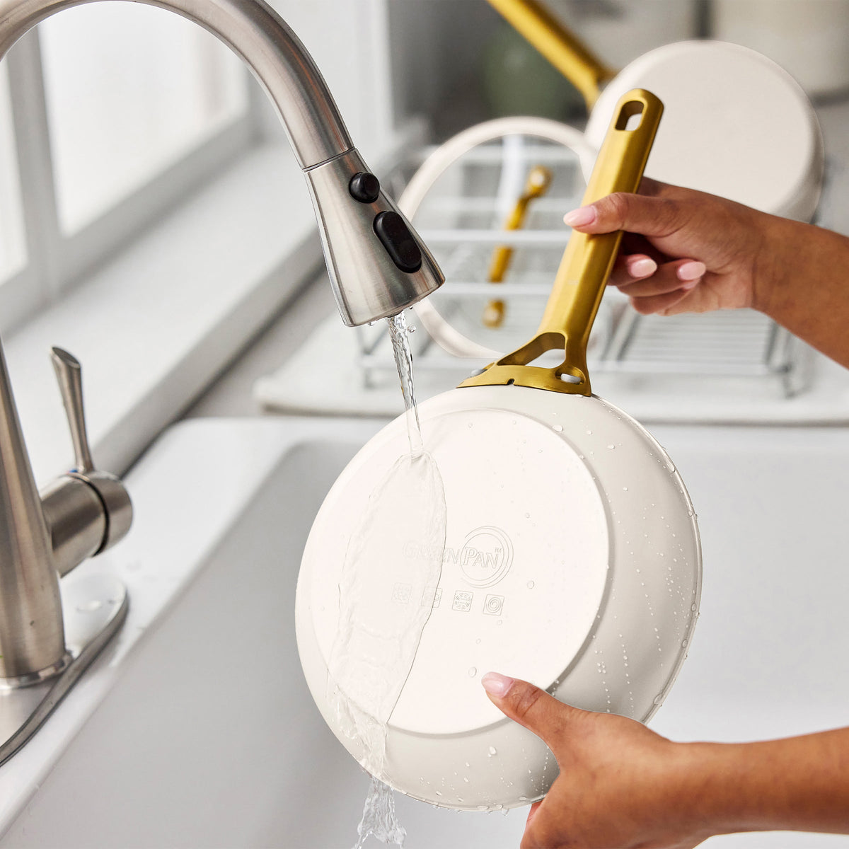 Person washing a cream frying pan with a gold handle in a kitchen sink.