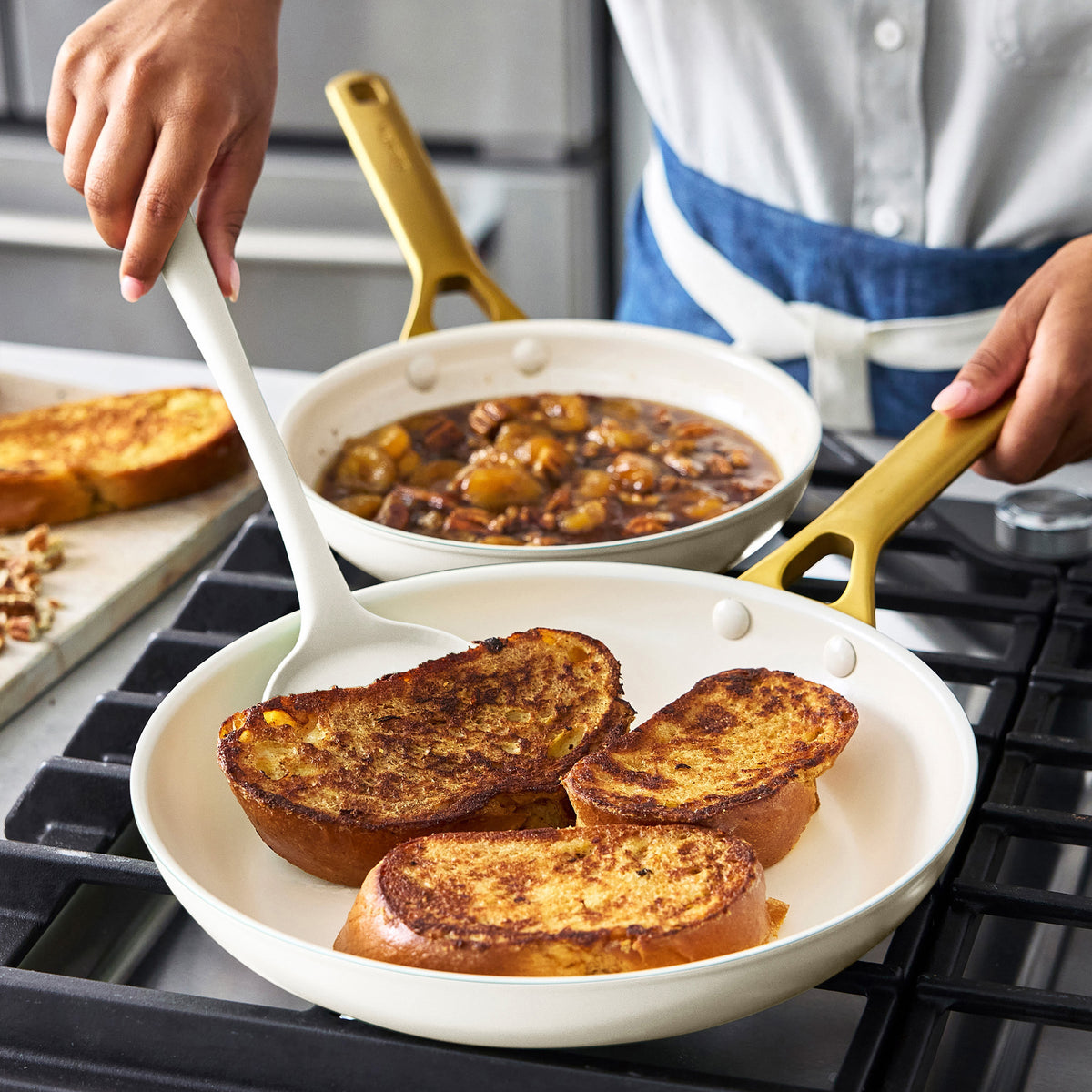 Person cooking French toast in a cream pan with gold handles on a stovetop.