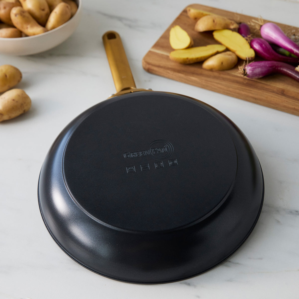 Black frying pan on a marble surface with potatoes and onions in the background