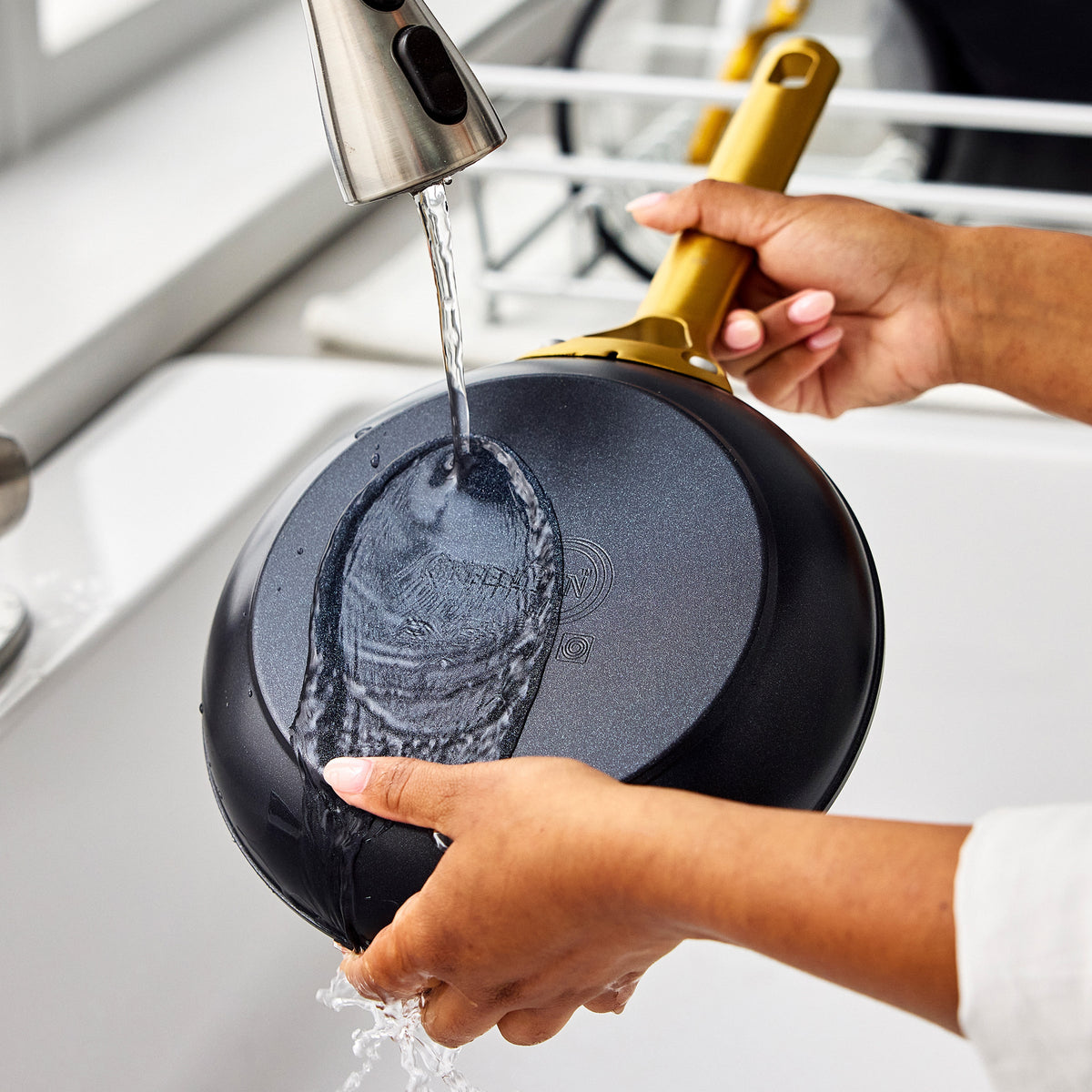 Person washing a black frying pan in a kitchen sink.