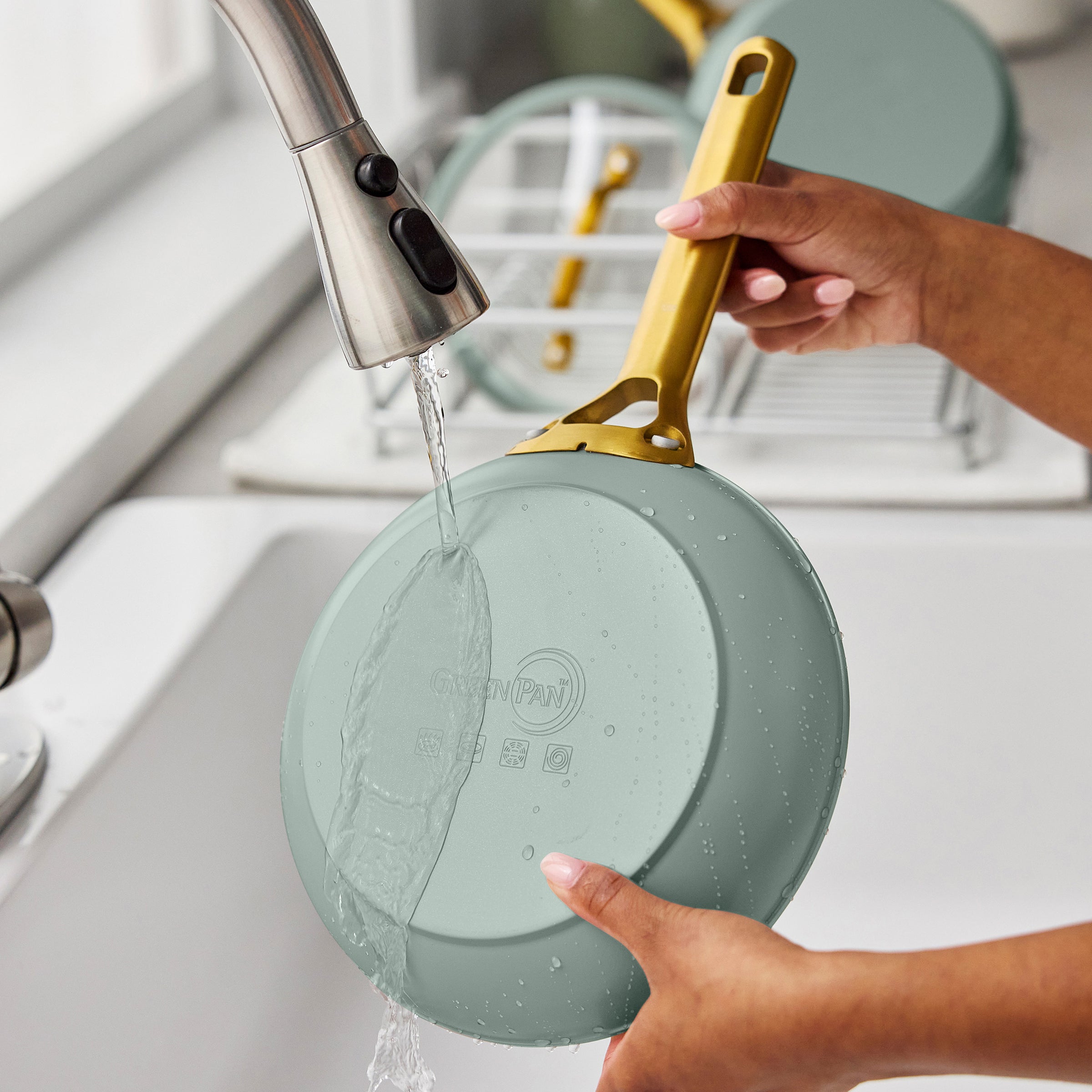 Person washing a green frying pan with a gold handle in a kitchen sink