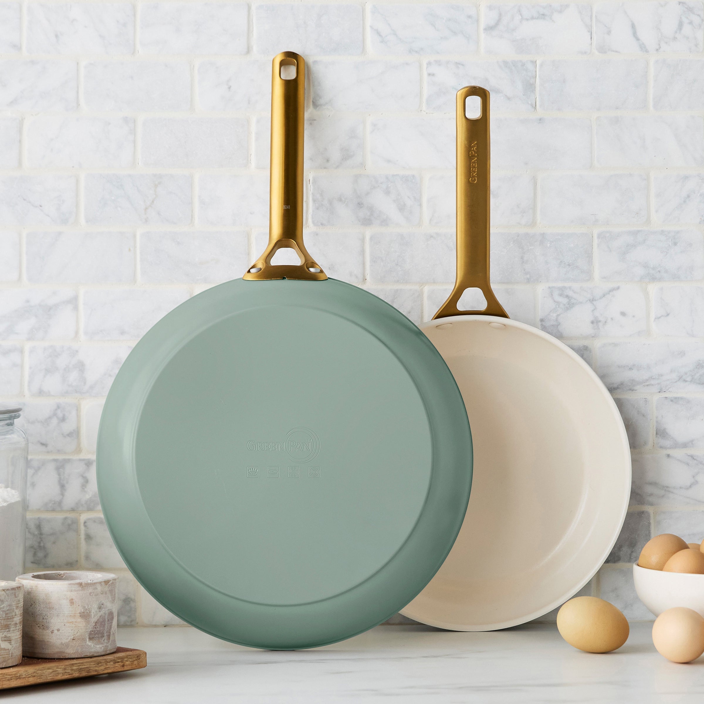 Two green frying pans with gold handles on a kitchen counter.