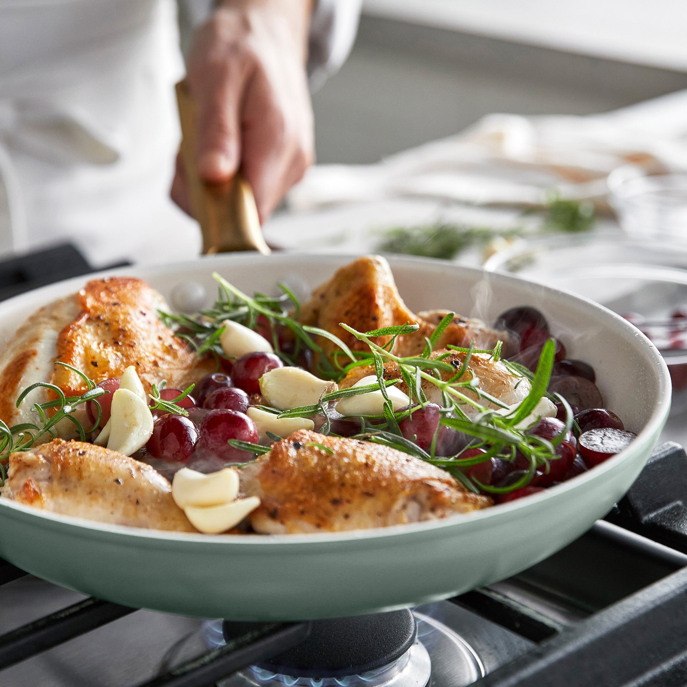 Chicken dish with grapes and herbs in a green frypan on a stove