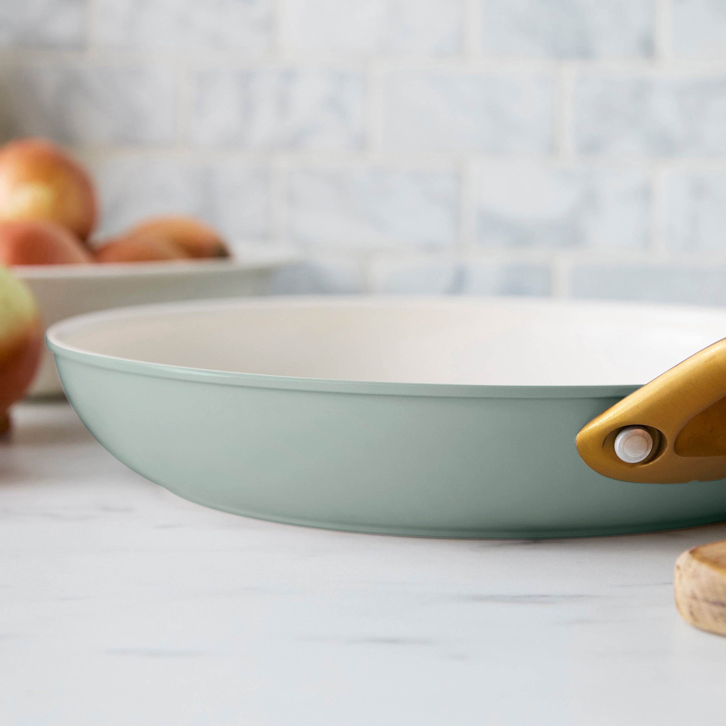 Green frying pan with a gold handle on a kitchen counter