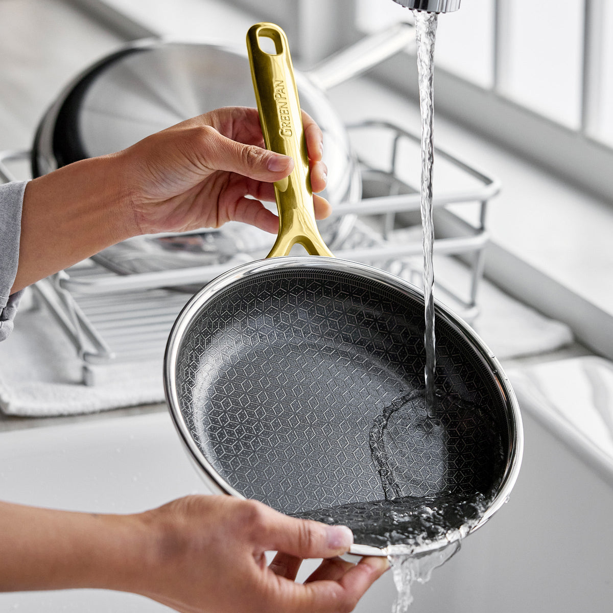 Person washing a gold hybrid ceramic nonstick frypan from a set of three by a window.