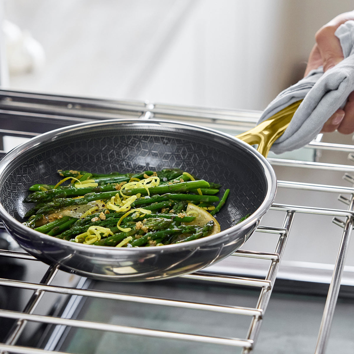 Hand holding a gold hybrid ceramic frypan with asparagus and lemon slices inside, ready to cook.