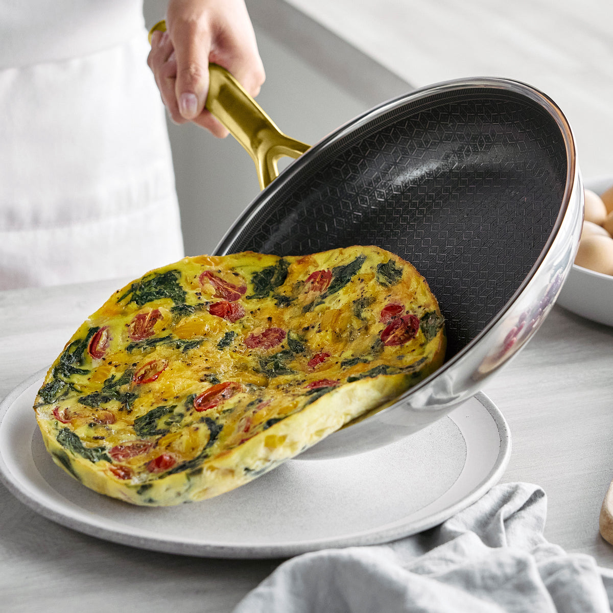A spinach and tomato frittata being slid from a Spectra Gold pan onto a plate on a kitchen counter.