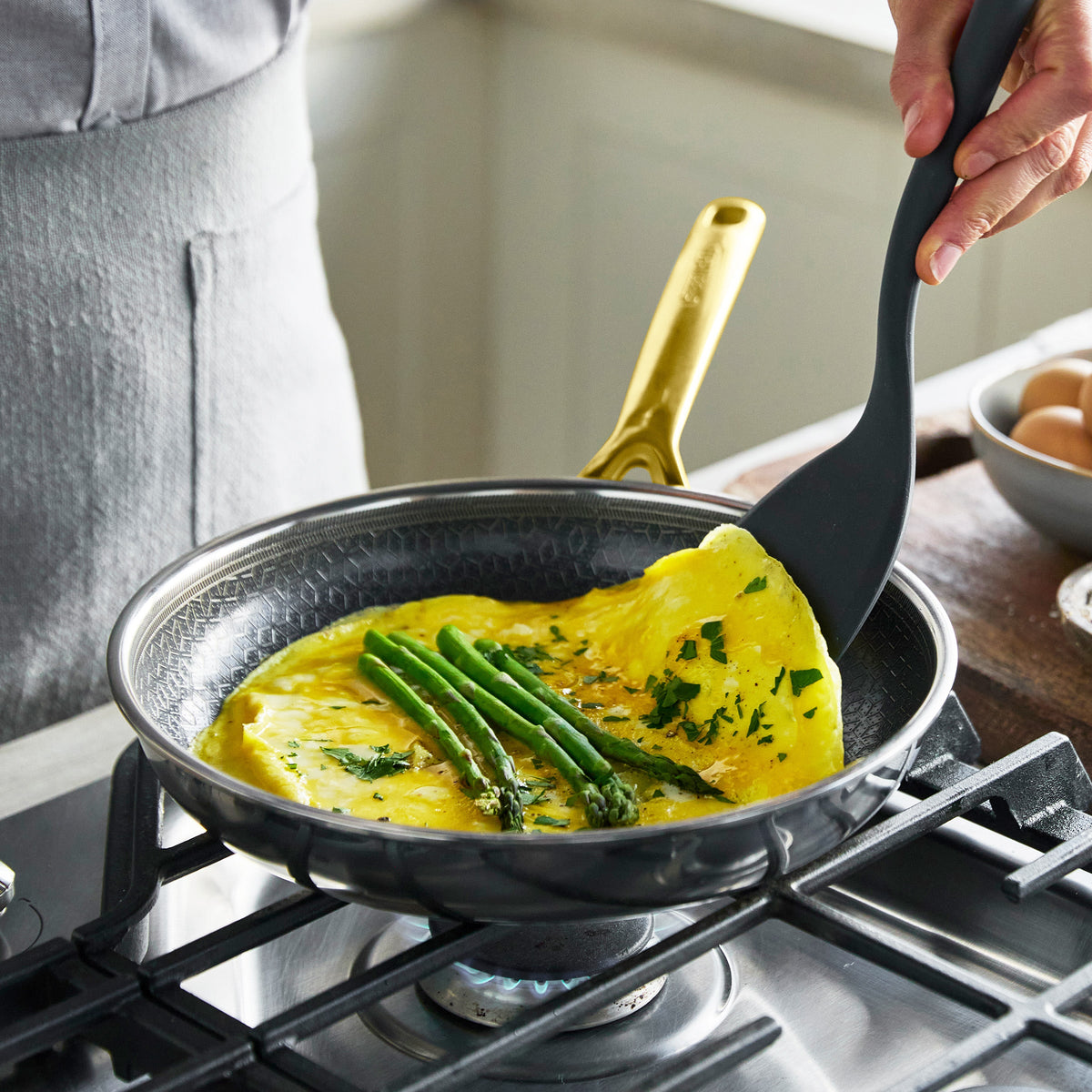 Gold hybrid ceramic nonstick pan on stove with asparagus omelet being folded inside.