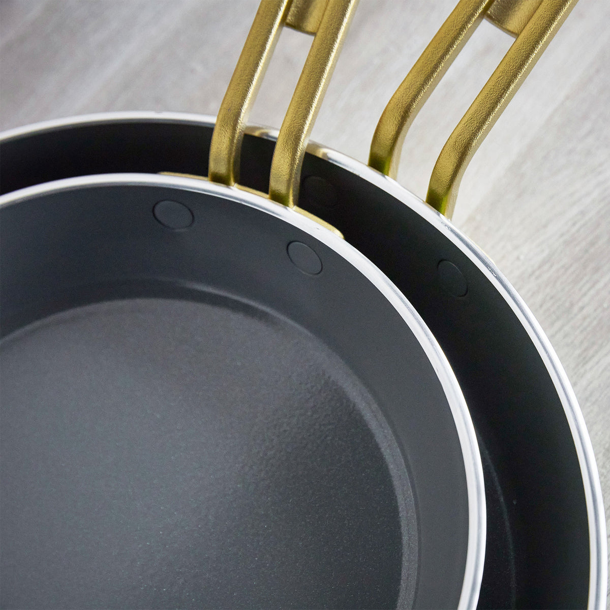 Frying pans with gold handles on a light wooden surface