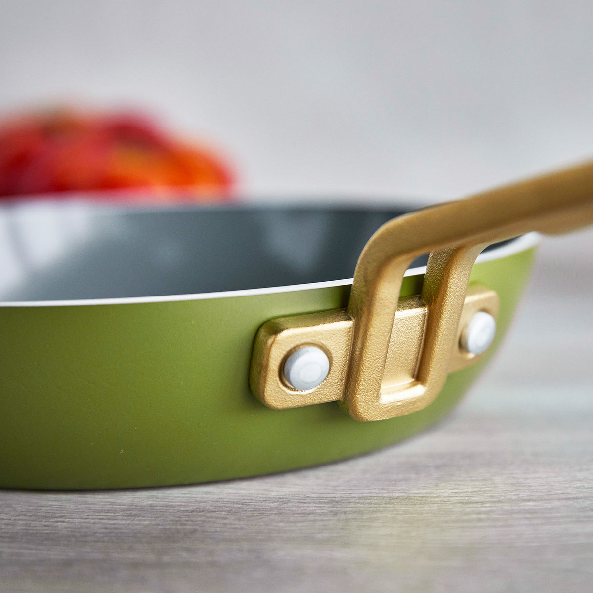 Close-up of a green frying pan with gold handles on a wooden surface.