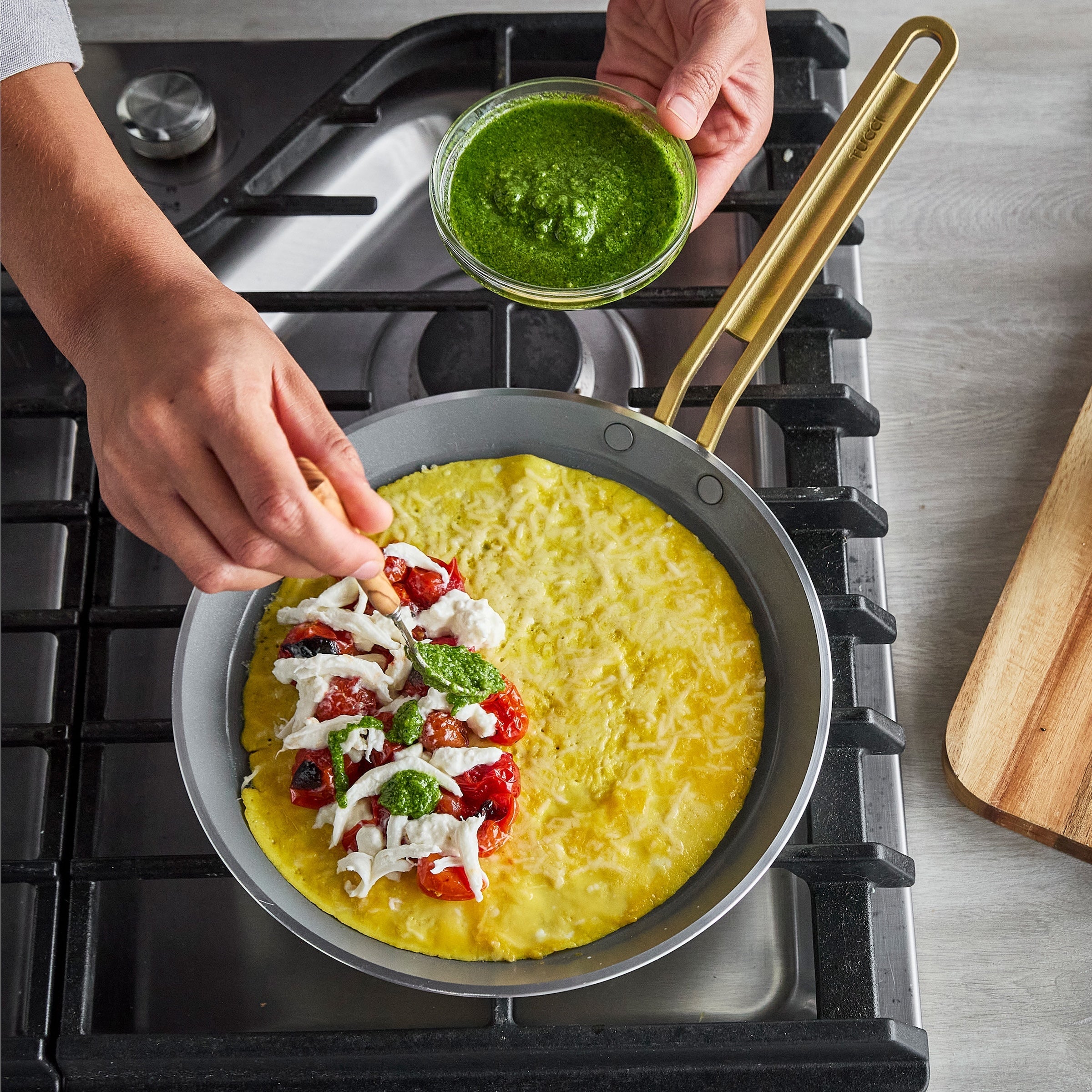 Person cooking a crepe on a stove with pesto being added.