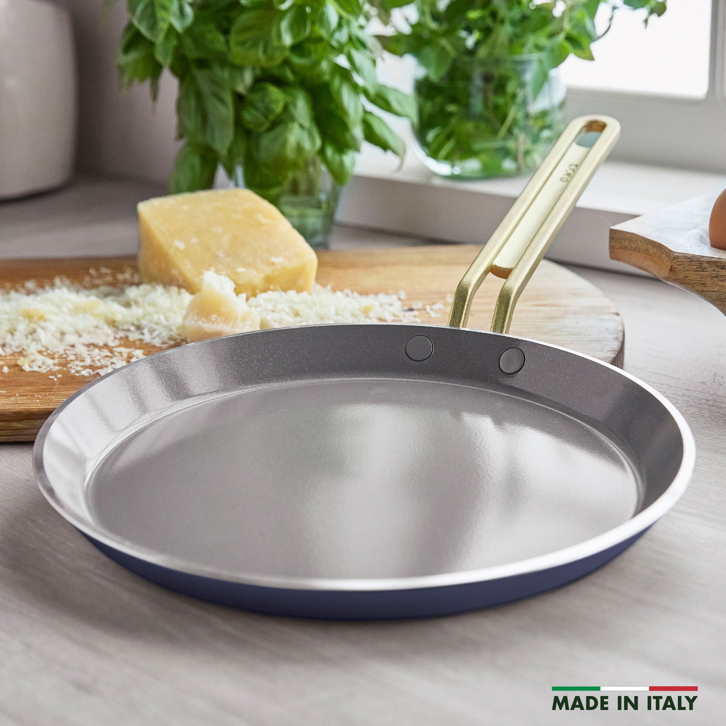 Crepe pan on a kitchen counter with cheese and herbs in the background