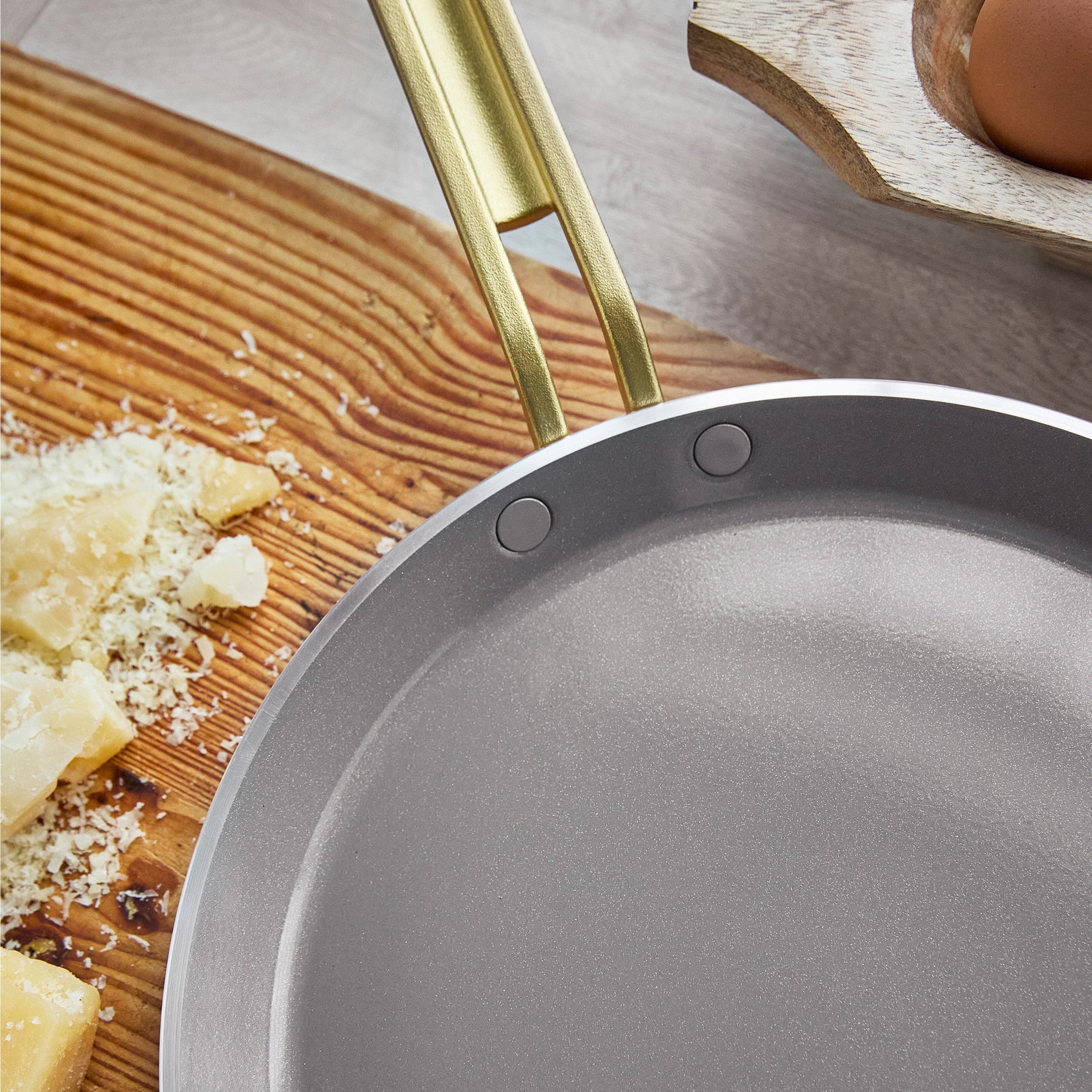 Crepe pan with a gold handle on a wooden cutting board with cheese and eggs.