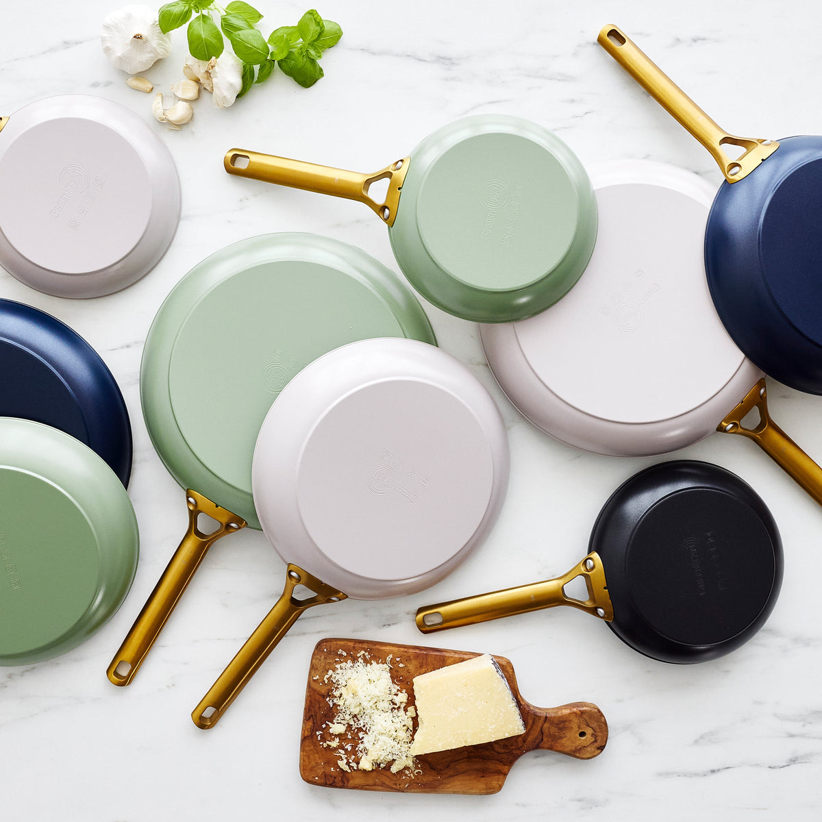 Set of colorful frying pans with gold handles on a marble surface.