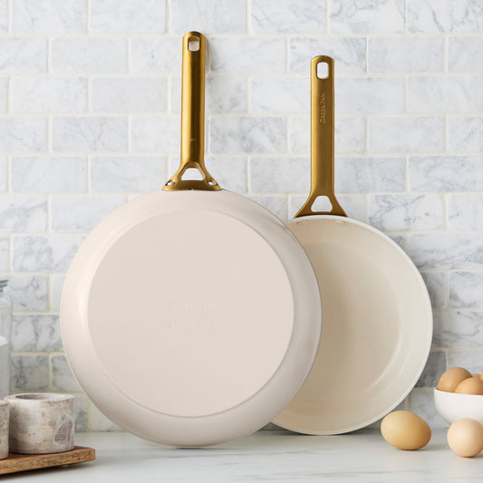 Two taupe frying pans with gold handles on a kitchen counter.