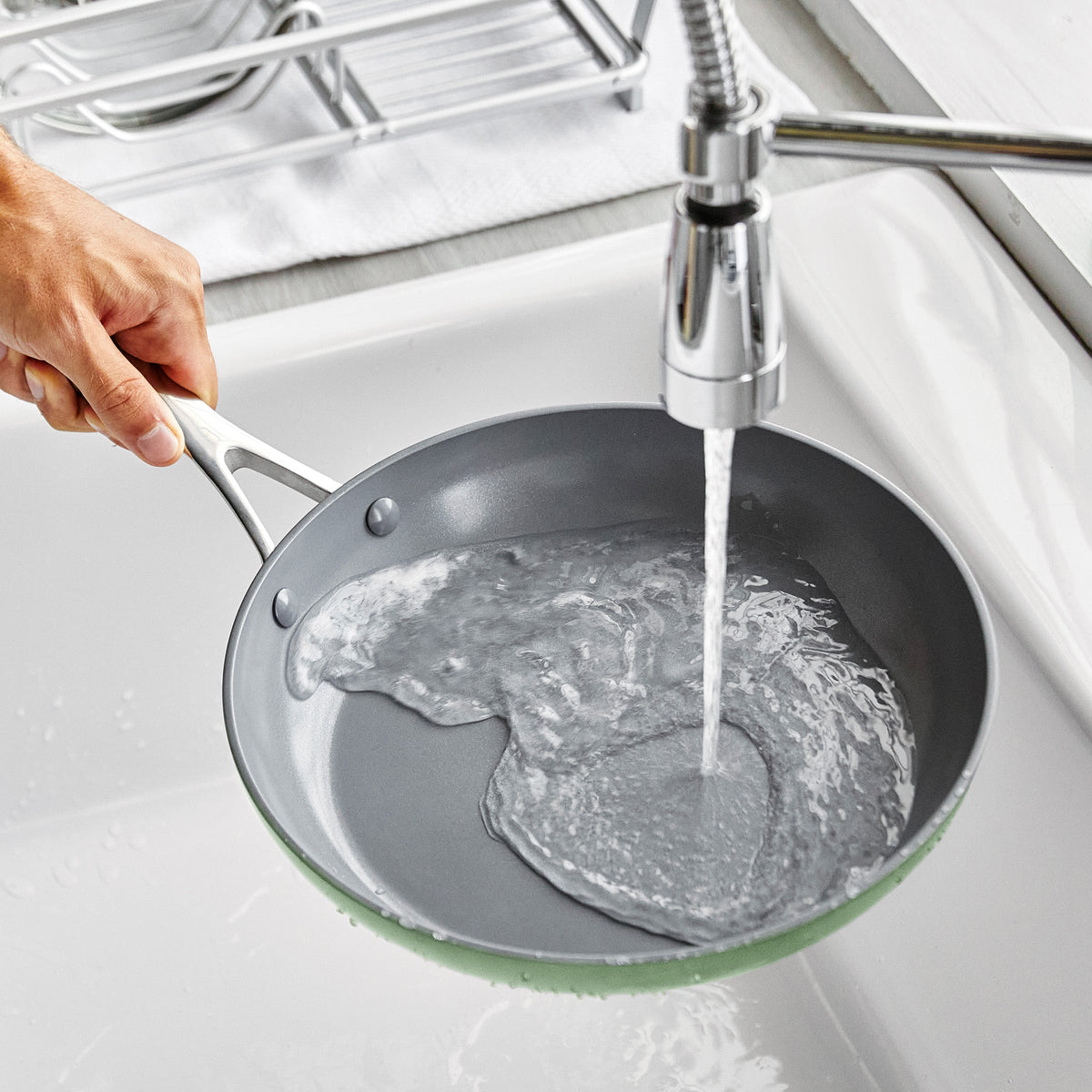 Person washing a frying pan under running water in a kitchen sink.