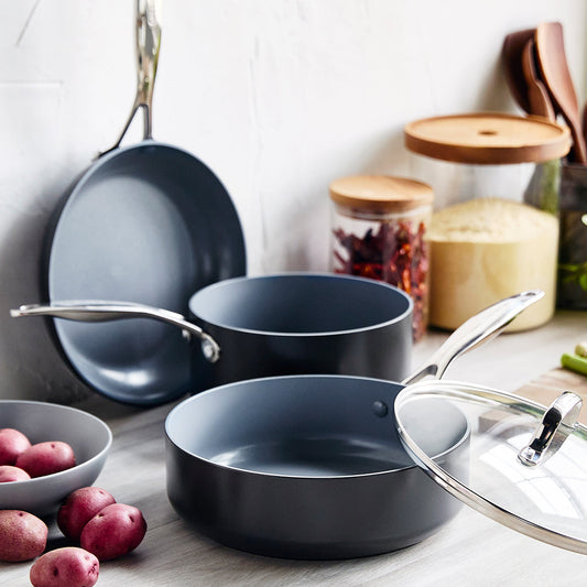 Set of black cookware on a kitchen counter with potatoes and jars in the background