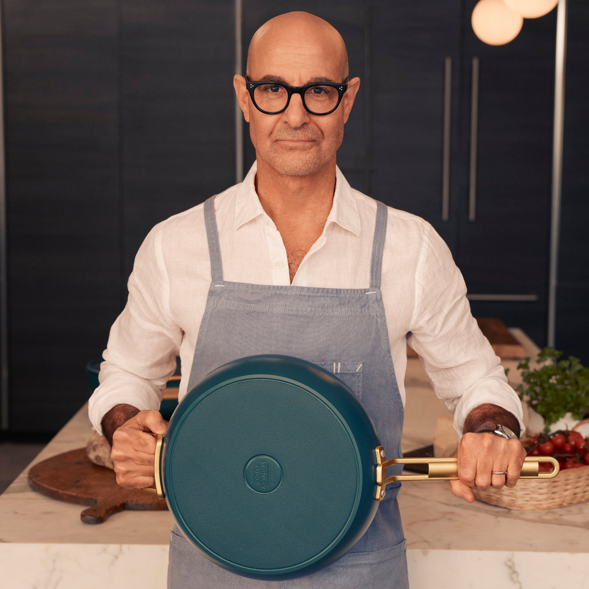 Stanley Tucci holding a teal saute pan in a kitchen 